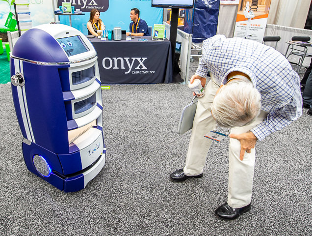 A trade show attendee checks to see if there is a person inside a robot roving around the show floor.