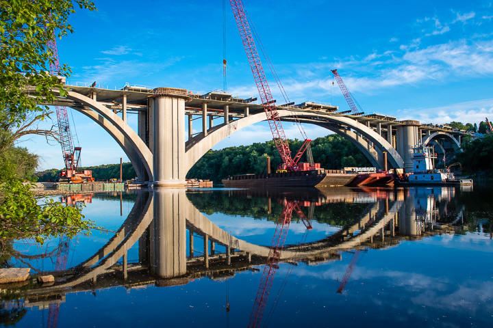 The Franklin Avenue bridge, and the equipment being used to rebuild it, are reflected in the Mississippi River.