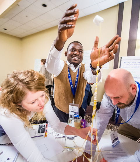 A team of conference attendees work to finish their spaghetti marshmallow tower.