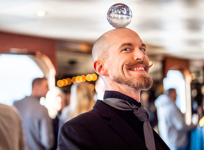 A juggler balances a glass ball on his head while performing on board a boat in San Francisco Bay for a corporate event.