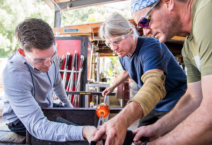A leadership conference attendee tries his hand at glass blowing with help from experienced glass blowers during a hosted activity in Laguna Beach, CA.