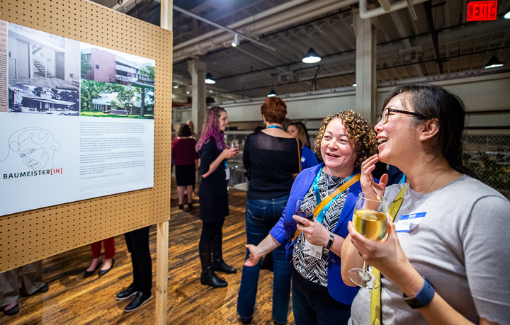At an off-site reception for women architects, two attendees discuss a colleague's project poster.