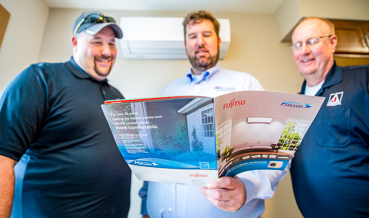 Contractors look over the product literature for the Fujitsu Halcyon mini split system installed behind them.