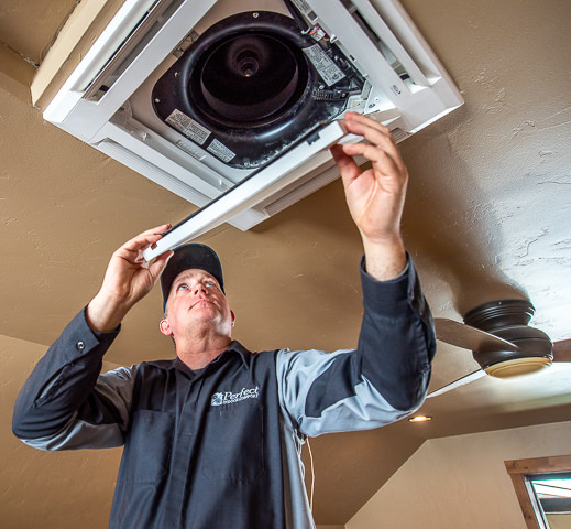 An HVAC technician installs a ceiling-mounted Fujitsu mini split unit for a residential project.