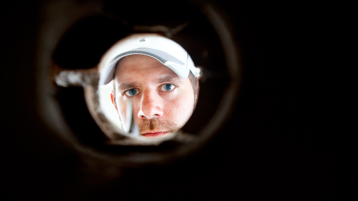 An HVAC installer looks through a hole he just drilled that will carry coolant lines and power.