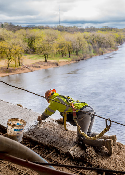 A worker attached to a safety line applies concrete to a span of the Franklin Avenue bridge in Minneapolis.